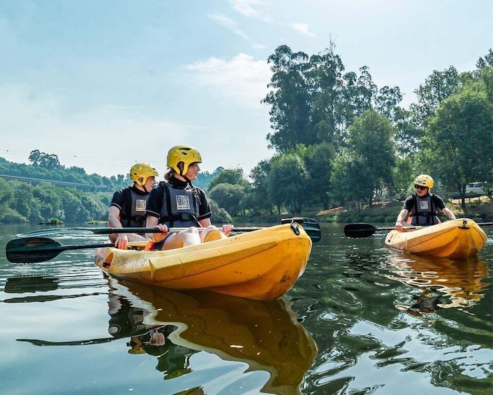 Drei Personen paddeln mit ihren Kajaks auf einem ruhigen Fluss, umgeben von Bäumen. 3