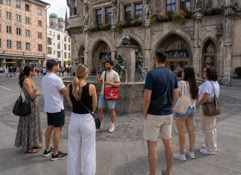 A group of people standing in front of a historical building with statues and a fountain. 1