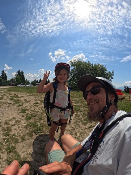 A person in a white shirt and cap, holding a camera, with a child in a floral backpack and helmet. 4