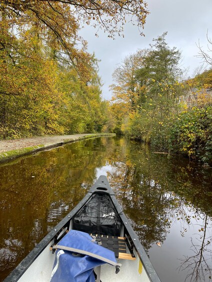 A narrow waterway flanked by trees with autumn foliage, a canoe with a blue cover on the seat, and a calm water surface reflecting the surroundings. 2