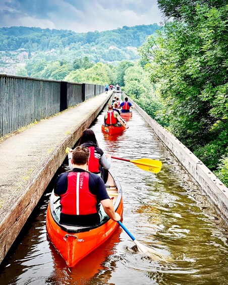 People paddling in red canoes on a narrow waterway with a bridge overhead. 3