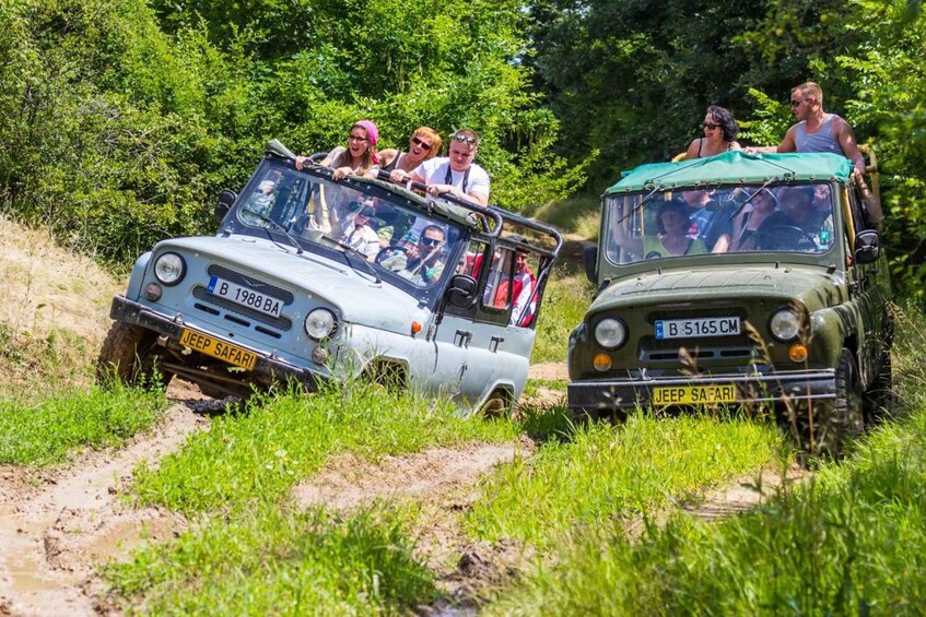 Two vintage cars on a muddy off-road trail with passengers. 1