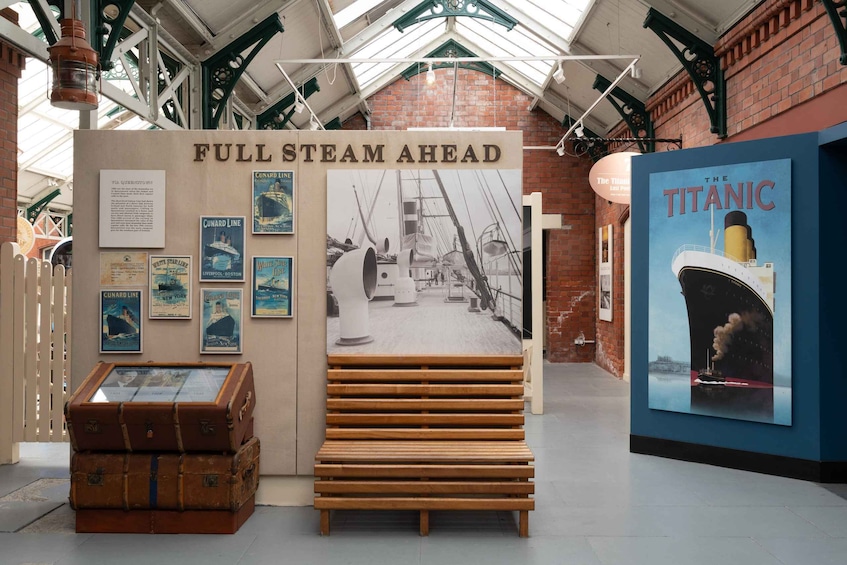 A museum exhibit with a 'FULLSTEAM AHEAD' sign, vintage posters, a large Titanic poster, and a wooden bench. 3