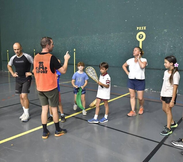 A group of people on a sports court, some holding tennis rackets, with a wall marked 'PAST' and a number '7'. 5