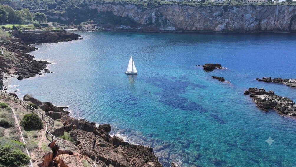 A sailboat on a clear blue sea with rocky shores and cliffs in the background. 5