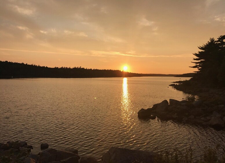 A sunset over a calm lake with a forested shoreline and rocks in the foreground. 3