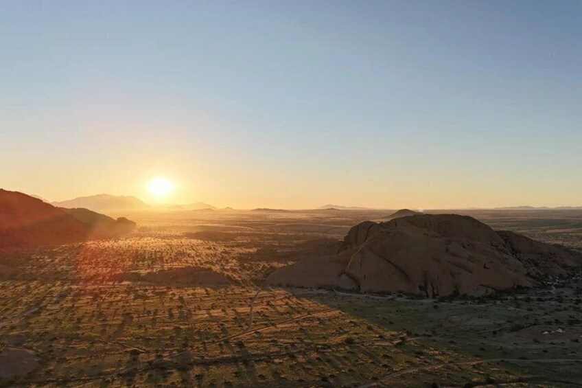 A desert landscape with a large rock formation and a city in the distance during sunset. 5