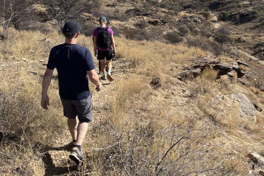 Two people hiking on a dry, rocky trail with sparse vegetation. 5