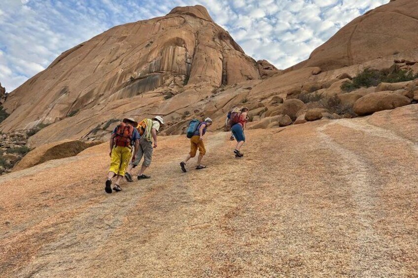 Hikers on a rocky trail with large rock formations in the background. 3