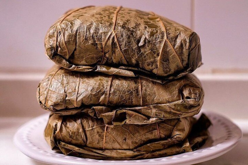 A stack of tamales wrapped in leaves on a white plate. 3