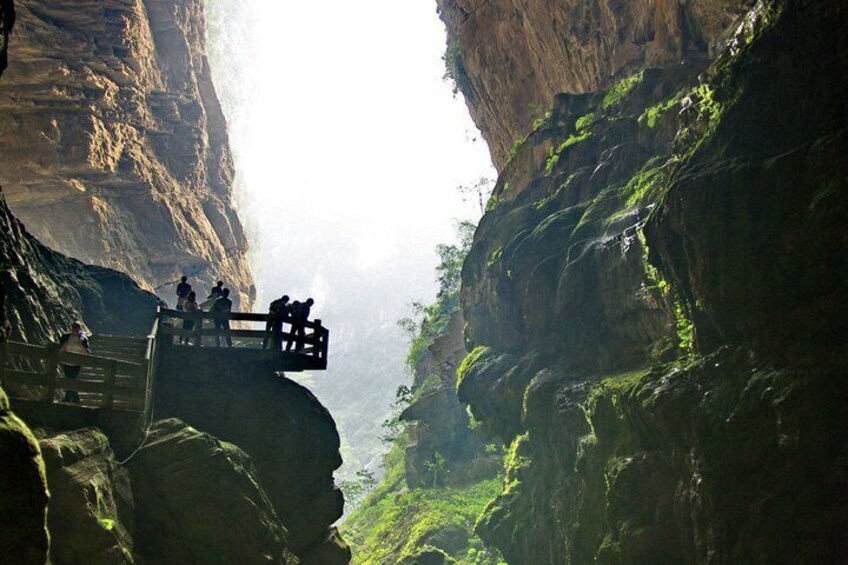 A wooden viewing platform overlooking a canyon with lush greenery and rocky cliffs. 3