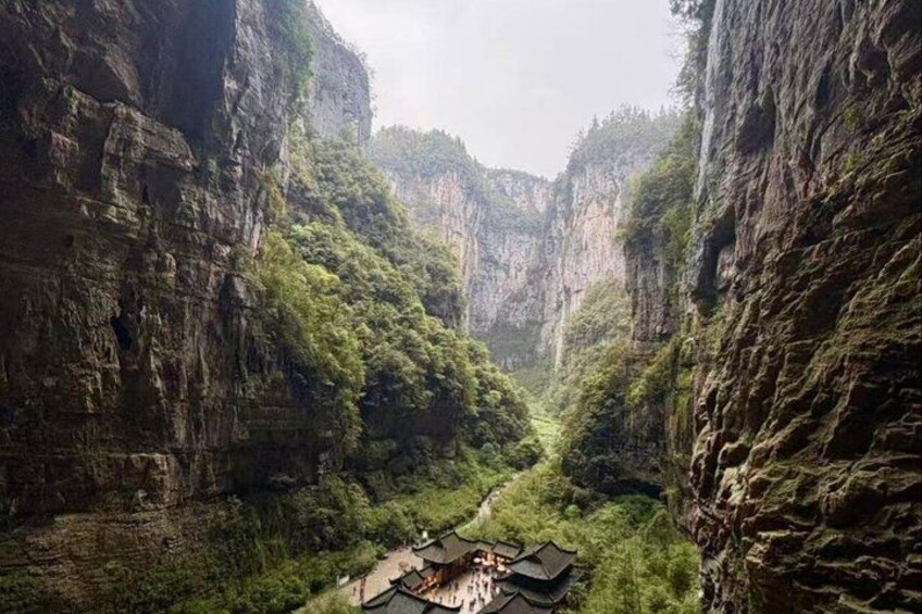 A narrow canyon with steep cliffs and a traditional building at the bottom. 3