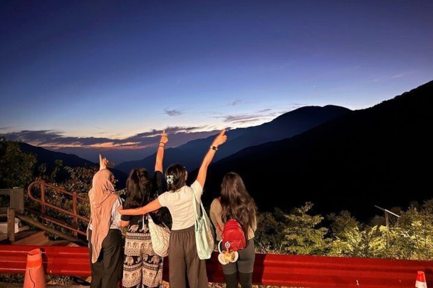 A group of people standing on a red railing, overlooking a mountainous landscape during twilight. 4