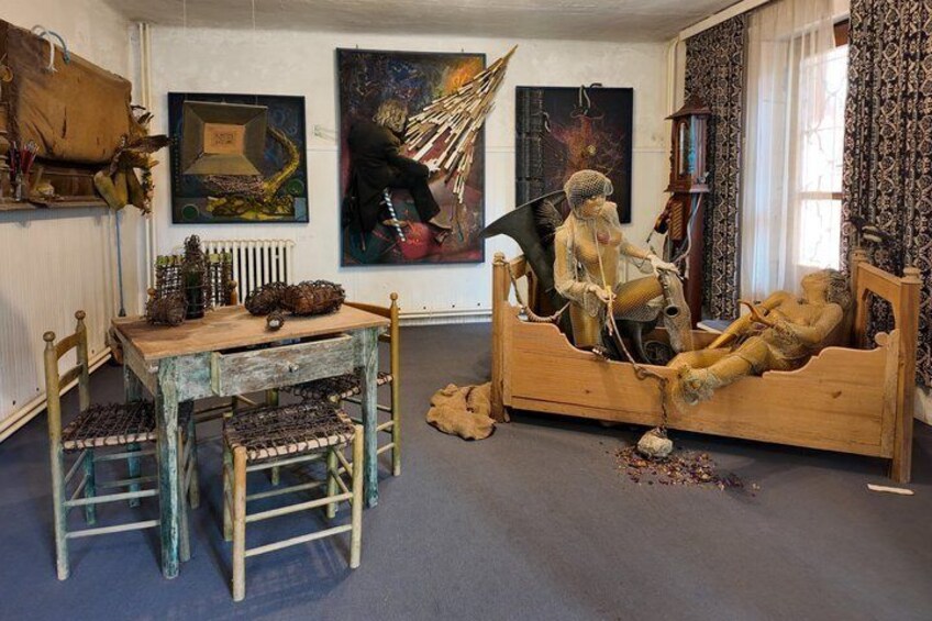 A room with a wooden bed, a table with chairs, and various artworks on the walls. 5