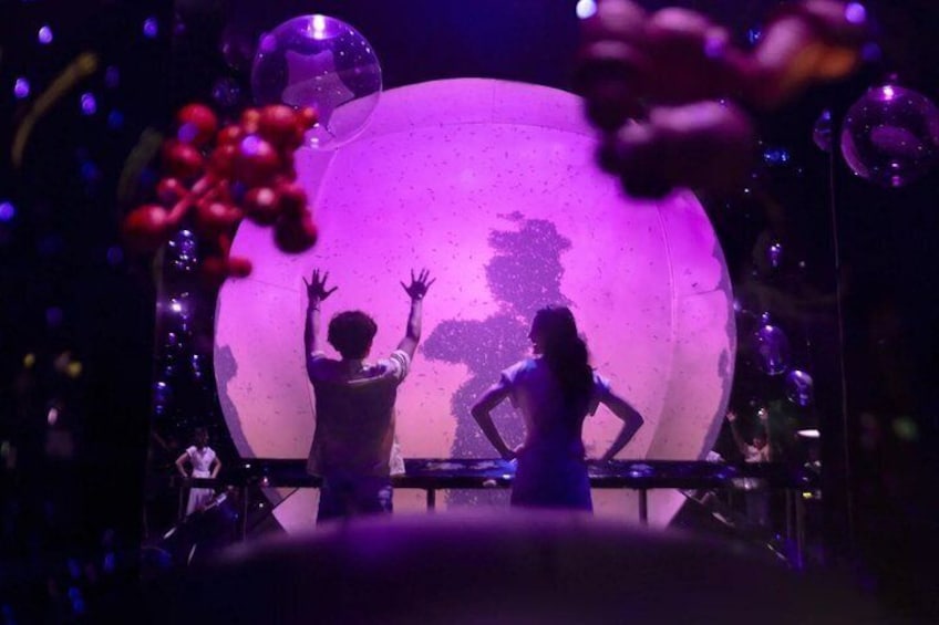 A stage with a large illuminated globe, a person with raised hands, and another person standing with hands on hips. 5
