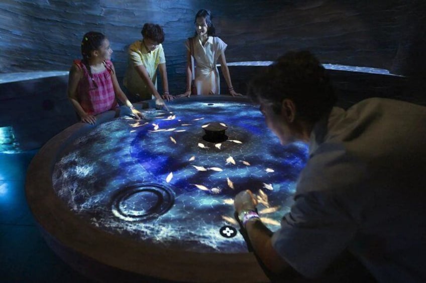 A group of people around a circular, illuminated water feature with fish swimming inside. 2