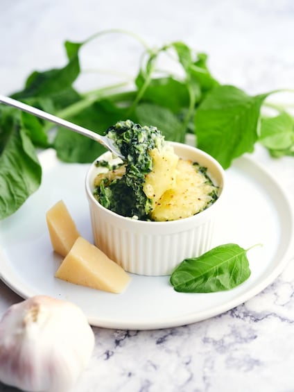 A dish with greens and potatoes, a spoon, and some garlic. 5