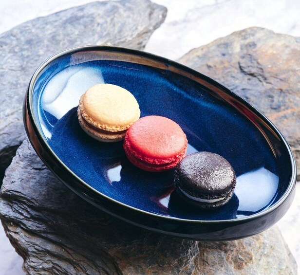 A blue ceramic dish with three macarons on a rock surface. 3