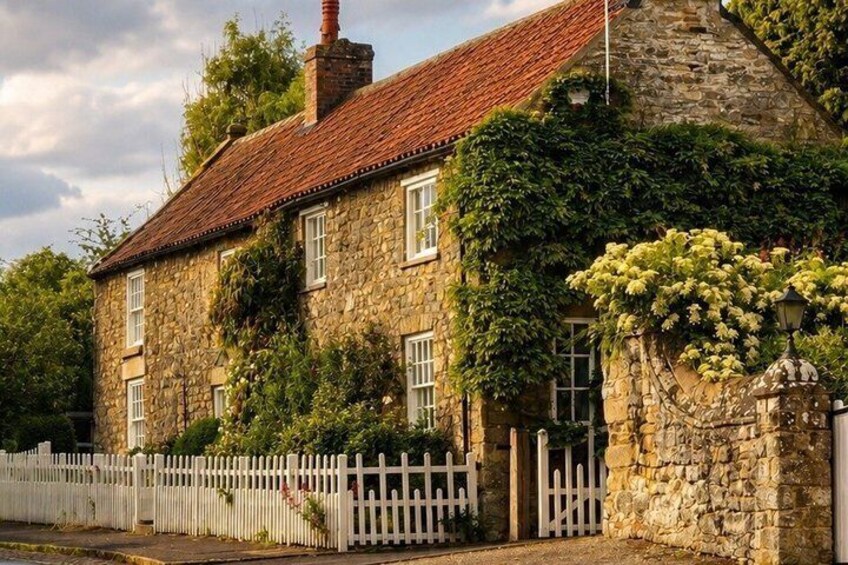 A stone house with a red tiled roof, white picket fence, and ivy-covered walls. 2