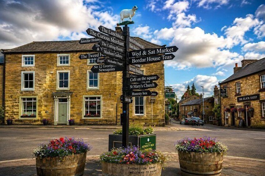 A street with a directional signpost, buildings, and flower pots. 1