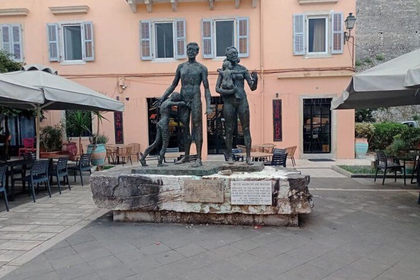 A statue of two figures on a stone pedestal in an outdoor setting with a building in the background. 3