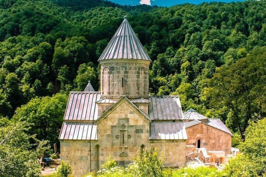 A stone church with a bell tower, surrounded by lush green forest. 3