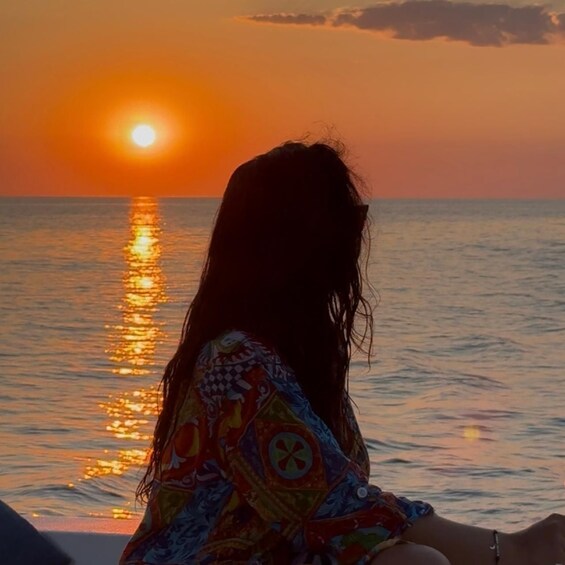 A person sitting by the ocean during sunset. 3