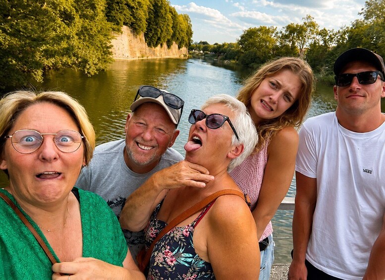 A group of people near a river with trees and a rocky bank in the background. 5