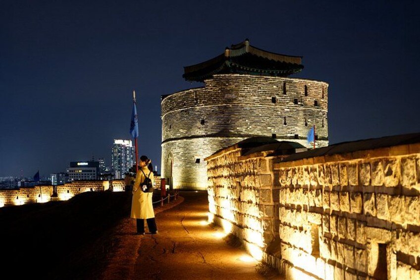 A historic stone wall with a person standing in front of a round tower at night. 5
