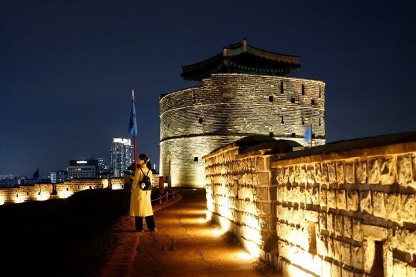 A historic stone wall with a watchtower, a person holding a flag, and a cityscape in the background. 4