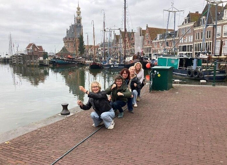 A group of people posing on a brick waterfront with boats and historic buildings in the background. 2