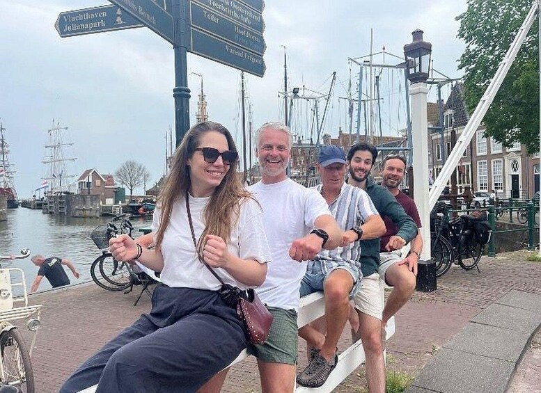 A group of people sitting on a bench by a canal with a signpost in the background. 1