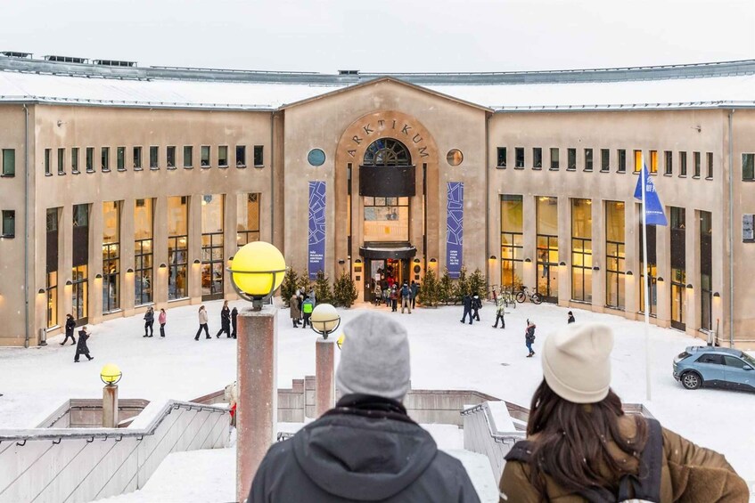 A building with a large entrance, people walking around, and snow on the ground. 2