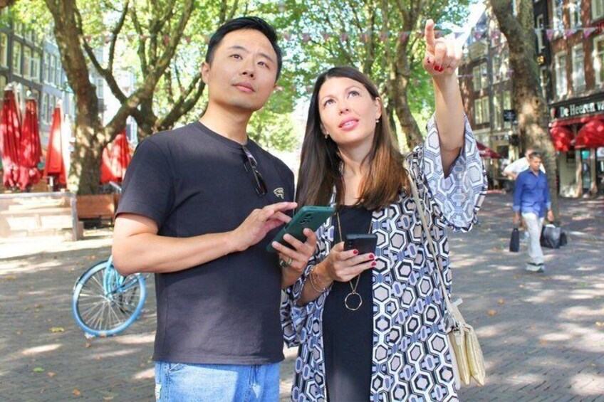 Two people standing on a cobblestone street, one holding a smartphone. 1