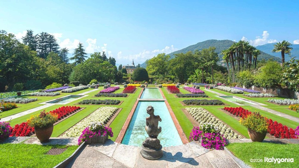 A formal garden with a central water feature, symmetrical flower beds, and a distant building. 1