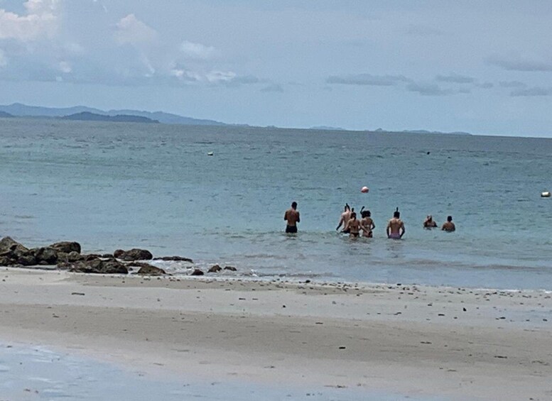 A beach with people swimming and playing in the water, with rocks and mountains in the background. 5
