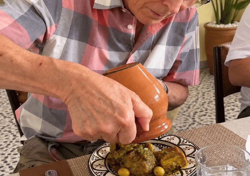 A person pouring sauce from a clay pot onto a plate with food. 3