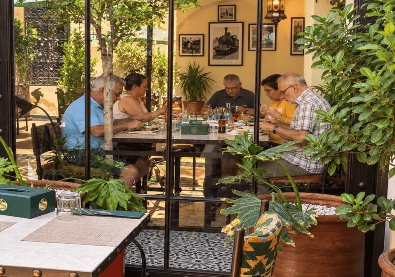 A group of people dining at an outdoor restaurant with potted plants and framed pictures on the walls. 4