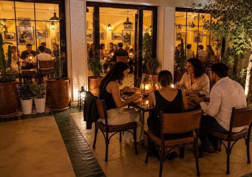 A group of people dining at an outdoor restaurant with large potted plants and warm lighting. 1