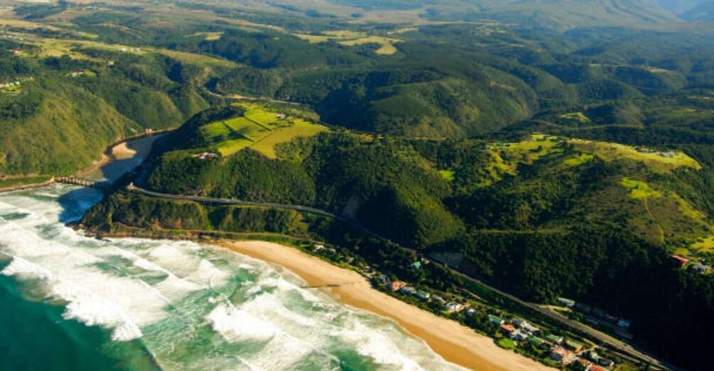 A coastal landscape with a beach, forested hills, and a winding road. 3
