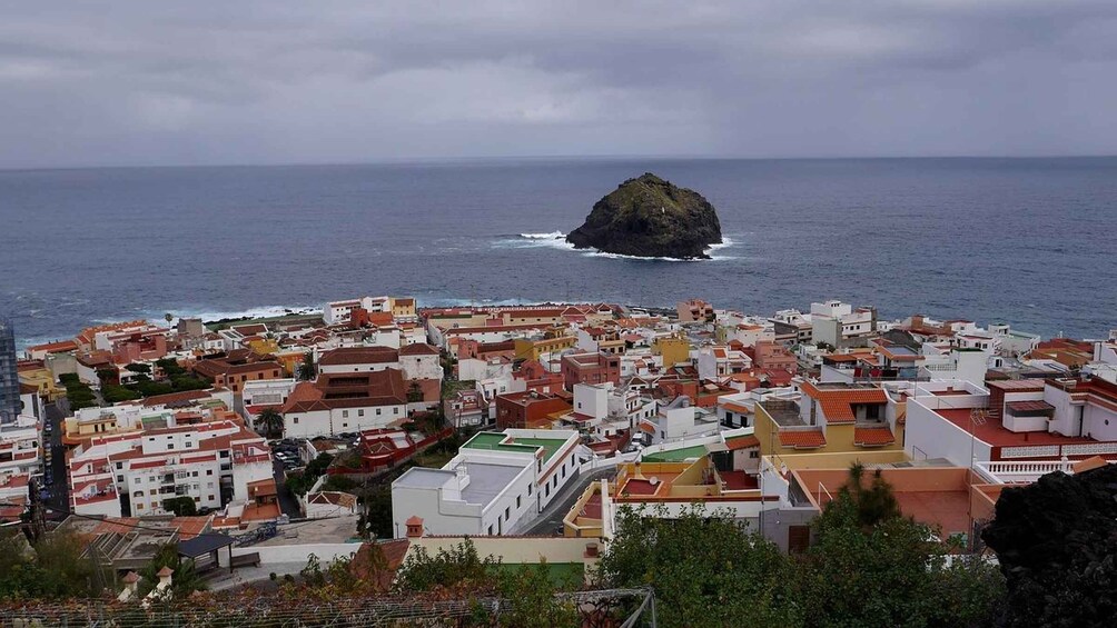 A coastal town with buildings and a prominent rocky island in the sea. 3