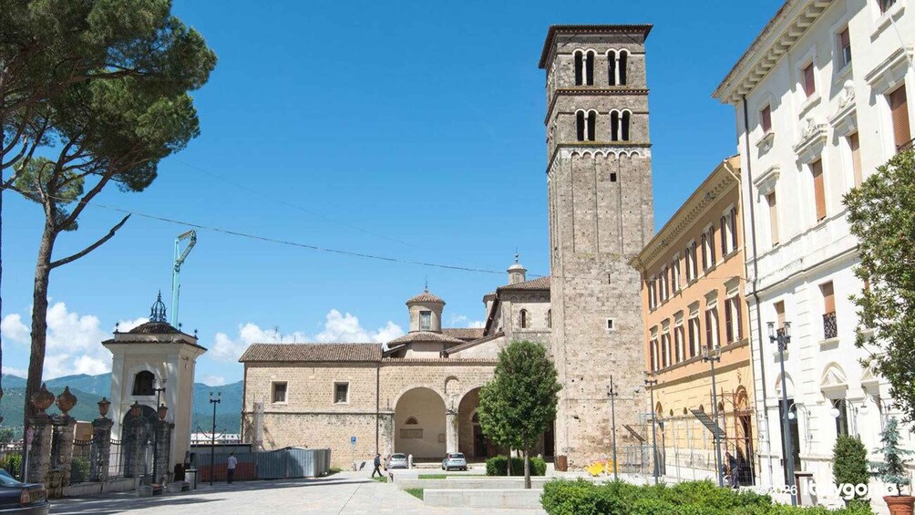 A historic square with a prominent church featuring a bell tower, surrounded by traditional buildings and a clear blue sky. 1