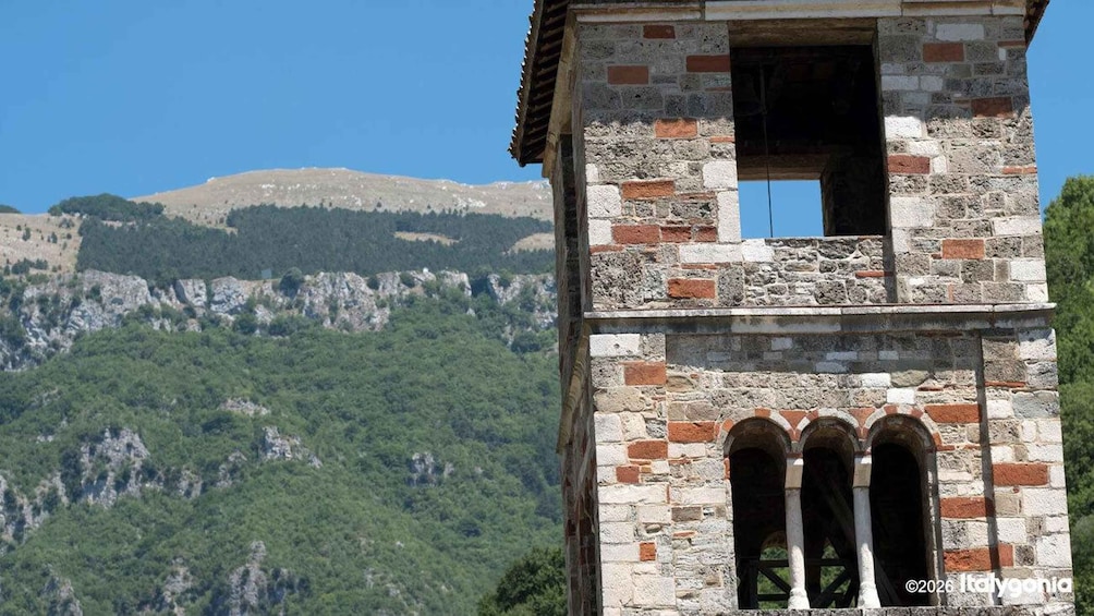 A stone tower with arched windows and a small balcony, set against a mountainous backdrop. 2