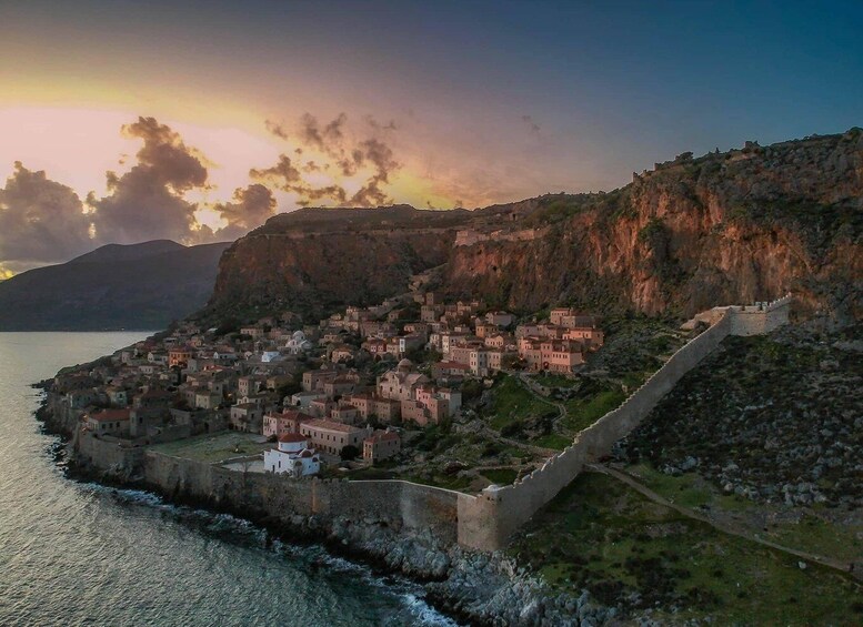 A coastal town with a fortified wall, houses, and a mountainous backdrop. 1