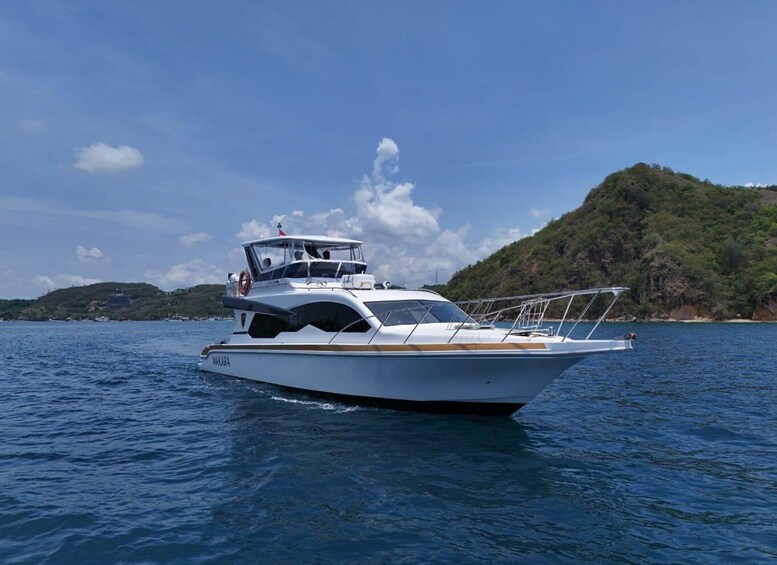 A white yacht named MAKARA on a calm sea with a mountainous coastline in the background. 1