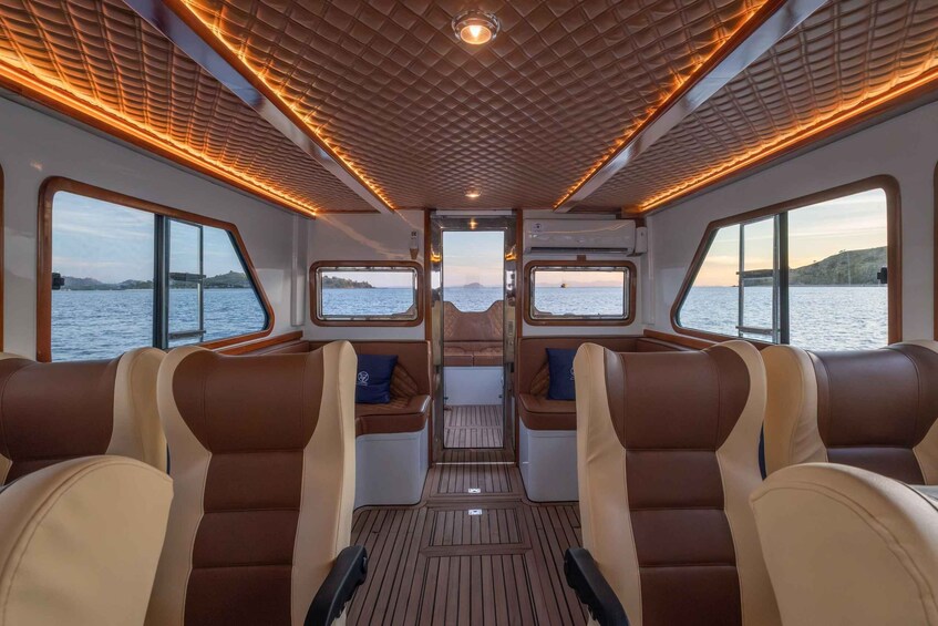 A boat interior with leather seating, wooden flooring, and large windows offering a view of the water. 4