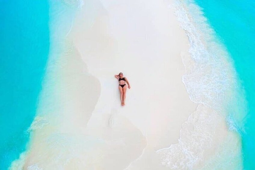 A person lying on a beach with clear turquoise water and white sand. 3