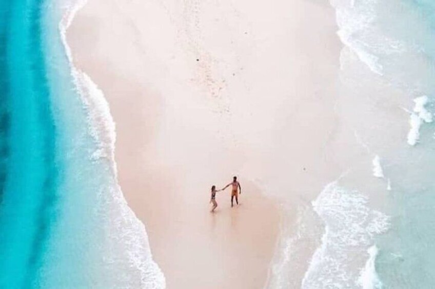 A sandy beach with gentle waves and two people holding hands walking along the shore. 2