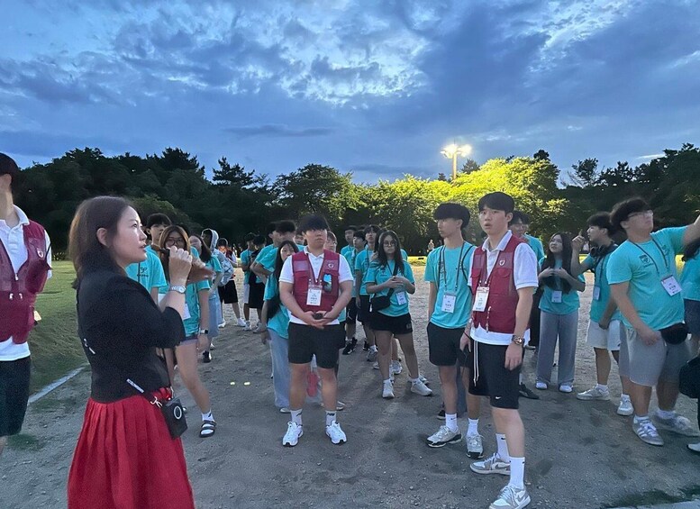 A group of people standing outdoors, some wearing vests, under a cloudy sky. 4