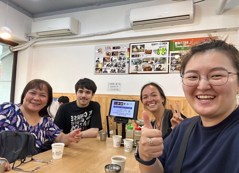 A group of people sitting at a table with coffee cups, a digital menu board, and a wall with various posters. 5